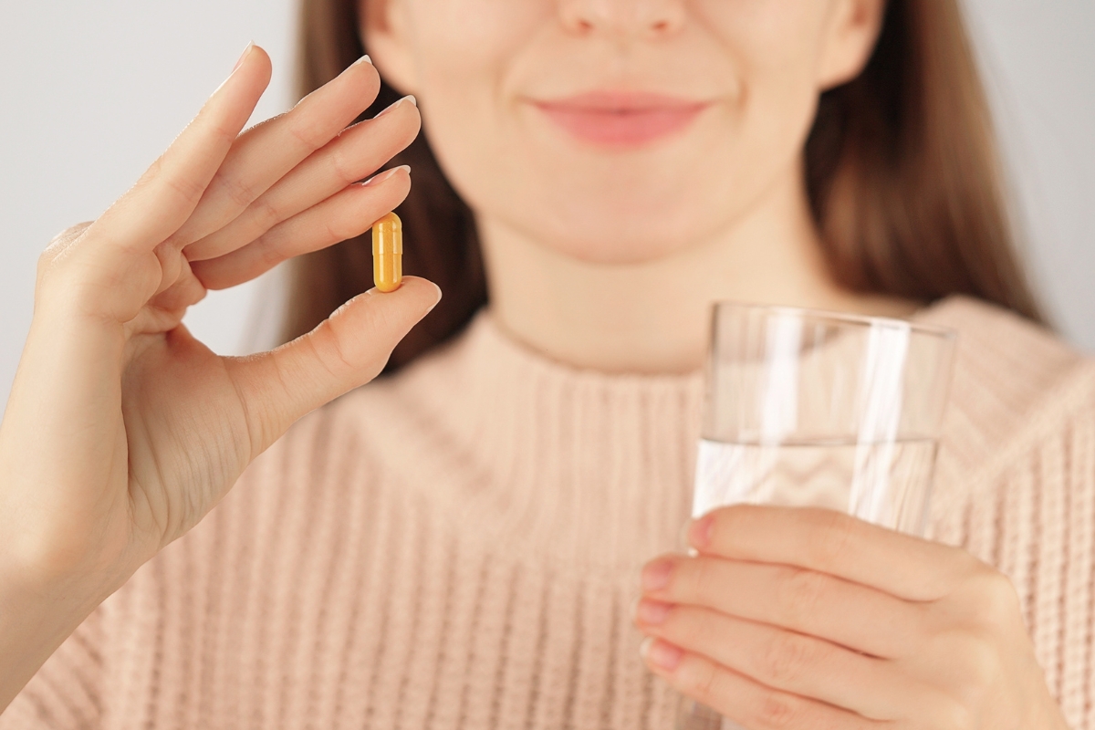 devojka drži čašu vode i kurkumin suplement u ruci